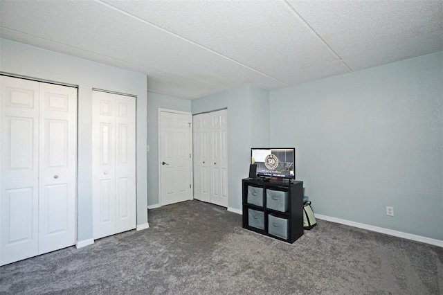 unfurnished bedroom featuring two closets, baseboards, and dark carpet