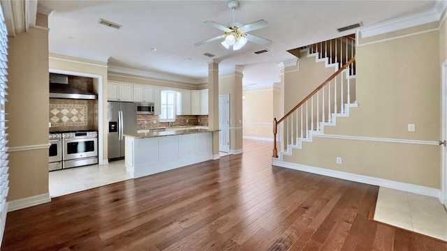 kitchen featuring light hardwood / wood-style floors, white cabinetry, wall chimney exhaust hood, appliances with stainless steel finishes, and ceiling fan