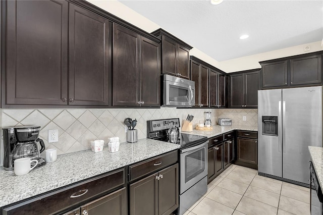 kitchen featuring tasteful backsplash, appliances with stainless steel finishes, dark brown cabinetry, light tile patterned floors, and light stone countertops