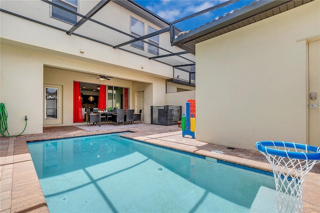 view of swimming pool featuring ceiling fan, glass enclosure, and a patio