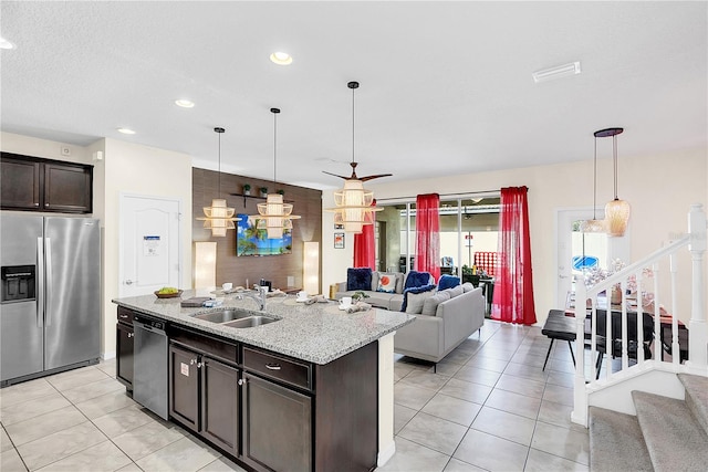 kitchen featuring a kitchen island with sink, sink, stainless steel appliances, decorative light fixtures, and dark brown cabinetry