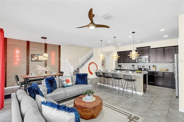 tiled living room with ceiling fan with notable chandelier