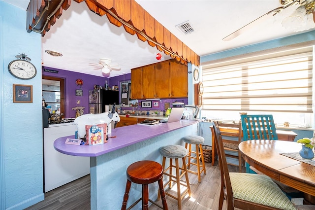 kitchen with dark hardwood / wood-style floors, a breakfast bar area, kitchen peninsula, ceiling fan, and refrigerator