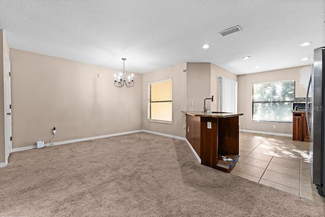 kitchen featuring a textured ceiling, sink, a notable chandelier, light colored carpet, and hanging light fixtures