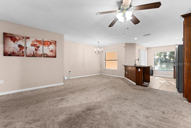 unfurnished living room featuring ceiling fan with notable chandelier, sink, and light colored carpet