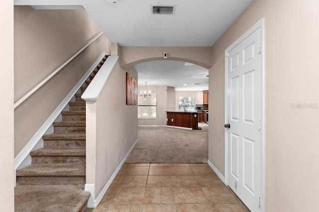 corridor with light carpet and an inviting chandelier