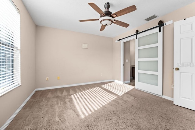 unfurnished bedroom featuring ceiling fan, carpet floors, and a barn door