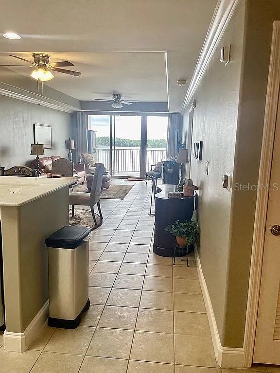 tiled living room with ceiling fan and crown molding