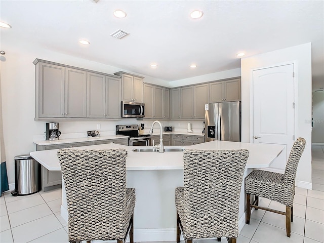 kitchen featuring light tile patterned flooring, sink, a kitchen island with sink, stainless steel appliances, and a breakfast bar area