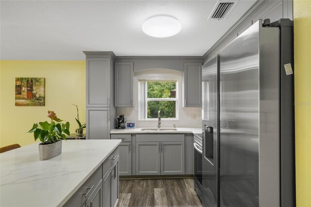 kitchen featuring light stone countertops, dark wood-type flooring, decorative backsplash, sink, and stainless steel fridge with ice dispenser