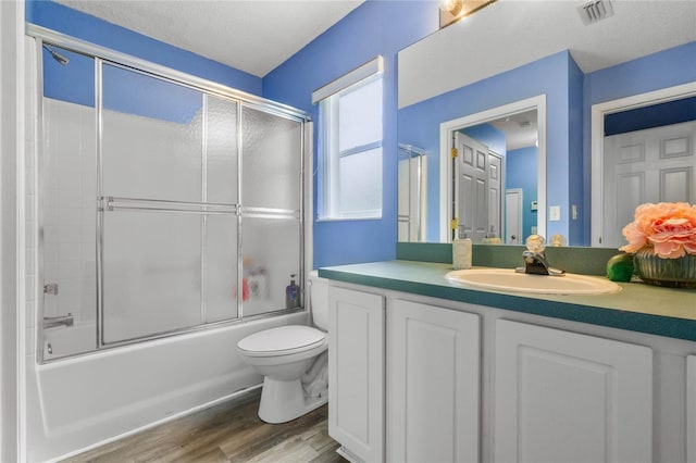 full bathroom featuring toilet, hardwood / wood-style floors, a textured ceiling, combined bath / shower with glass door, and vanity