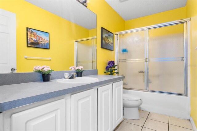 full bathroom featuring a textured ceiling, tile patterned flooring, vanity, bath / shower combo with glass door, and toilet