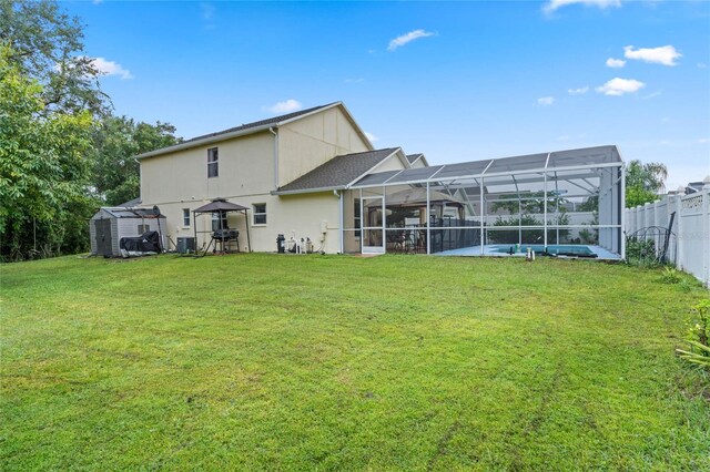 rear view of property with glass enclosure, a yard, and a storage shed