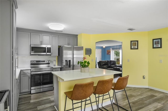 kitchen featuring appliances with stainless steel finishes, backsplash, gray cabinets, a kitchen island, and a breakfast bar area