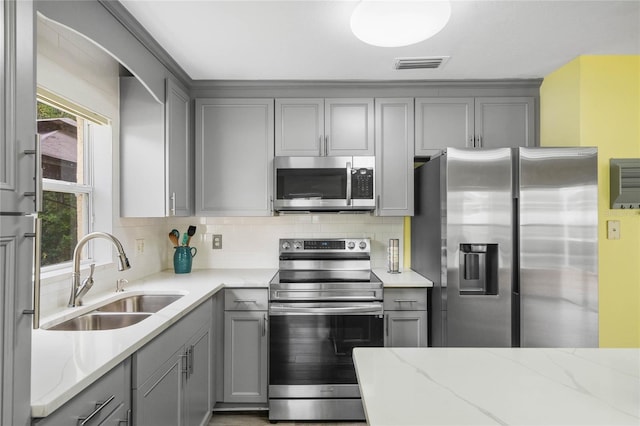 kitchen with sink, stainless steel appliances, light stone counters, and gray cabinetry