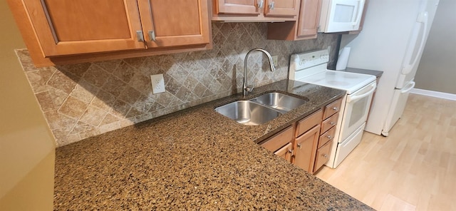 kitchen featuring decorative backsplash, dark stone countertops, sink, light wood-type flooring, and white appliances