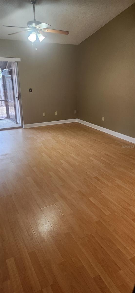 spare room with ceiling fan, a textured ceiling, vaulted ceiling, and light wood-type flooring