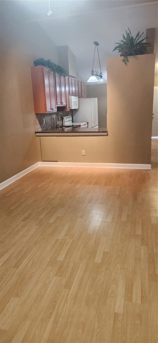 interior space with white appliances, sink, kitchen peninsula, light hardwood / wood-style floors, and pendant lighting