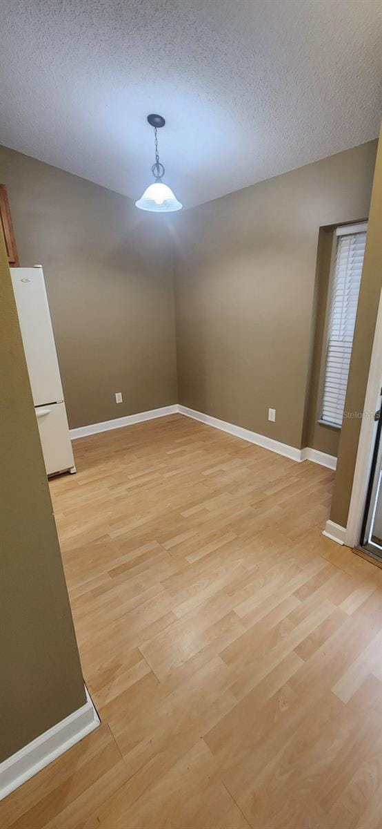 unfurnished dining area with a textured ceiling and light wood-type flooring