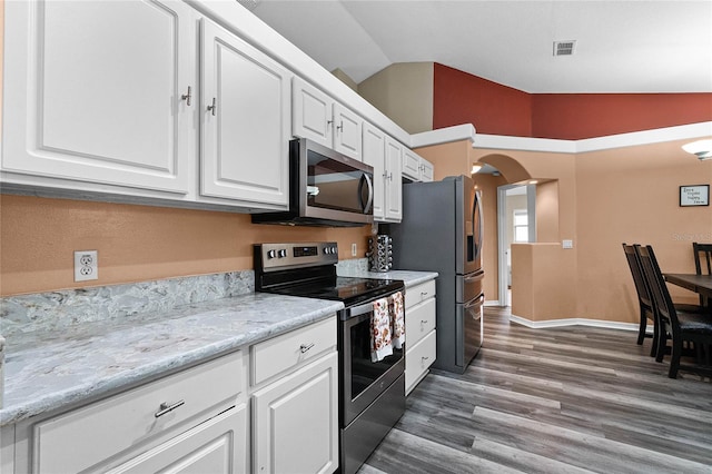 kitchen with dark wood-type flooring, vaulted ceiling, appliances with stainless steel finishes, light stone counters, and white cabinetry