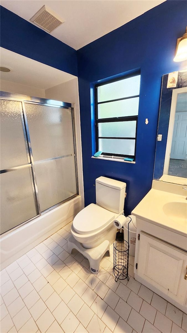 full bathroom with shower / bath combination with glass door, vanity, tile patterned flooring, and toilet