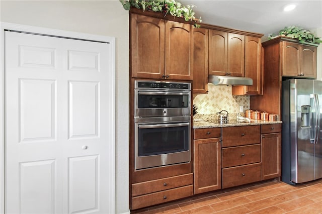 kitchen with light stone countertops, appliances with stainless steel finishes, light wood-type flooring, and decorative backsplash