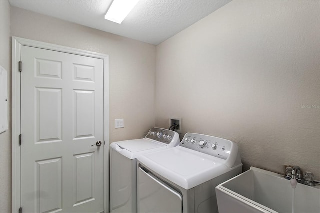 clothes washing area with separate washer and dryer, a textured ceiling, and sink