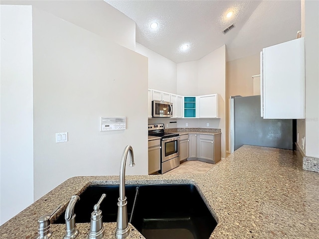 kitchen with light stone counters, appliances with stainless steel finishes, a textured ceiling, white cabinetry, and sink