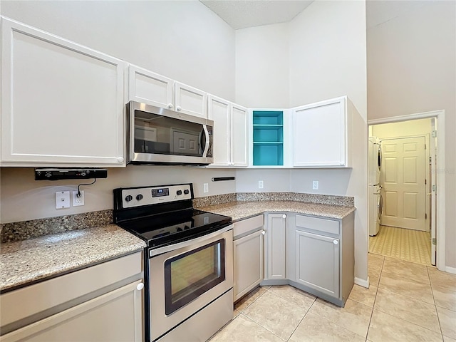 kitchen with light stone countertops, white cabinetry, light tile patterned floors, appliances with stainless steel finishes, and a towering ceiling