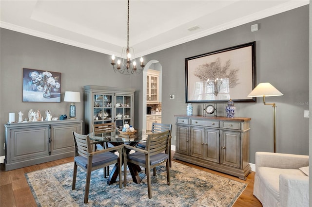 dining room with a raised ceiling, ornamental molding, a chandelier, and hardwood / wood-style flooring