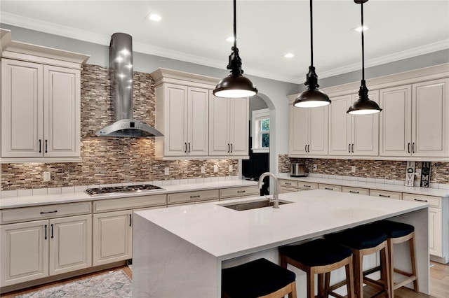 kitchen with wall chimney exhaust hood, light wood-type flooring, decorative light fixtures, a center island with sink, and sink