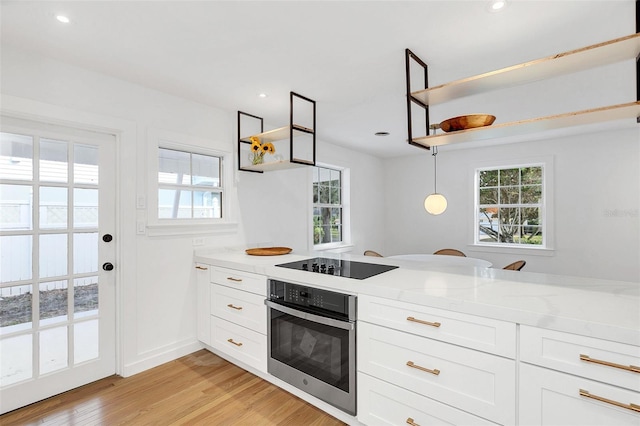 kitchen with stainless steel oven, white cabinets, hanging light fixtures, light hardwood / wood-style flooring, and light stone counters