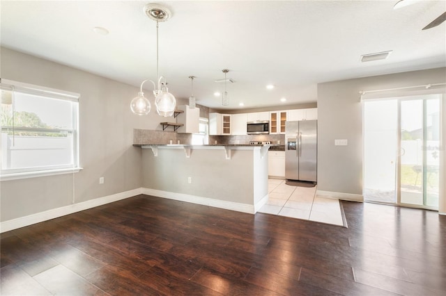 kitchen with kitchen peninsula, hanging light fixtures, white cabinetry, stainless steel appliances, and a breakfast bar