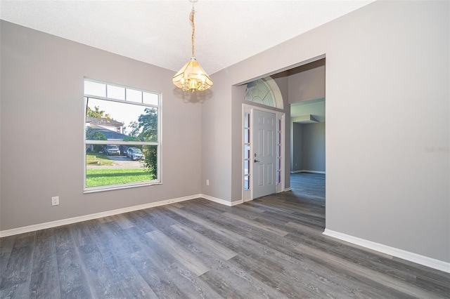 empty room with a notable chandelier, dark wood-type flooring, and a textured ceiling