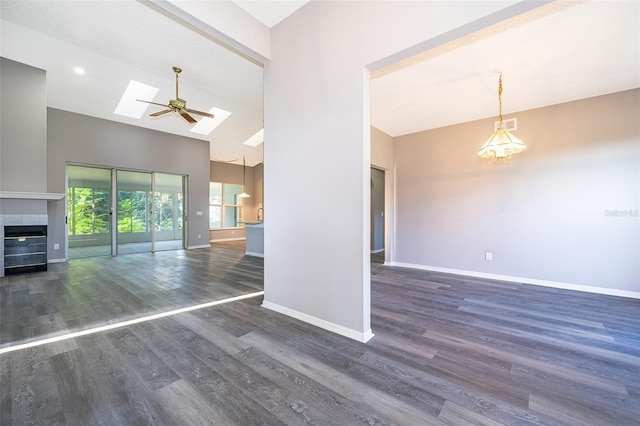 unfurnished room featuring a tile fireplace, dark hardwood / wood-style floors, ceiling fan, and a skylight