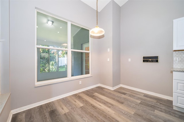 unfurnished dining area featuring vaulted ceiling and hardwood / wood-style flooring