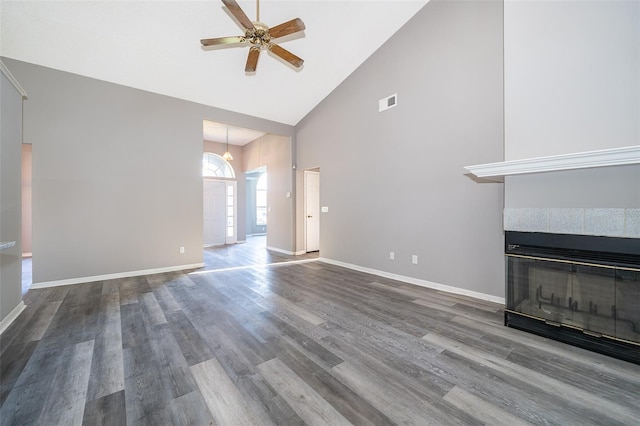 unfurnished living room featuring ceiling fan, hardwood / wood-style flooring, a tiled fireplace, and high vaulted ceiling