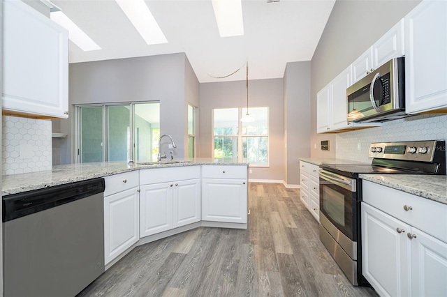 kitchen with white cabinets, a skylight, tasteful backsplash, light hardwood / wood-style flooring, and appliances with stainless steel finishes