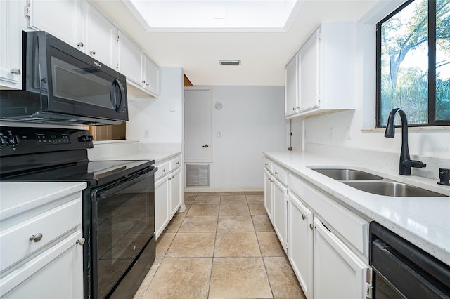 kitchen featuring light tile patterned flooring, a skylight, sink, white cabinetry, and black appliances