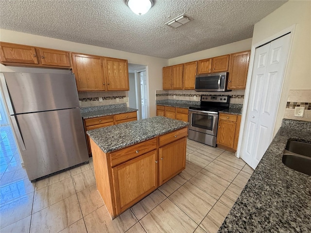 kitchen with decorative backsplash, appliances with stainless steel finishes, a textured ceiling, light tile patterned floors, and a center island