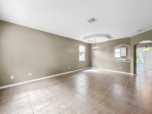 spare room with a textured ceiling, a healthy amount of sunlight, a chandelier, and tile patterned floors