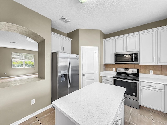 kitchen featuring light tile patterned flooring, white cabinets, a kitchen island, stainless steel appliances, and a textured ceiling