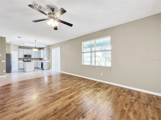 unfurnished living room with light hardwood / wood-style flooring, ceiling fan, and a textured ceiling