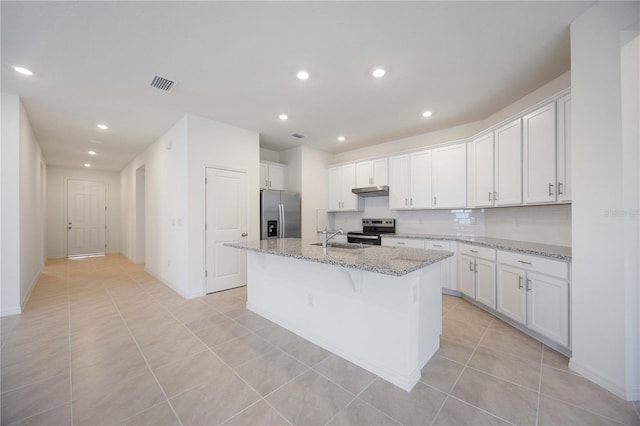 kitchen featuring light stone countertops, white cabinets, appliances with stainless steel finishes, and a kitchen island with sink