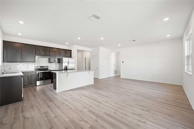 kitchen with light hardwood / wood-style flooring, stainless steel appliances, a center island, tasteful backsplash, and light stone countertops