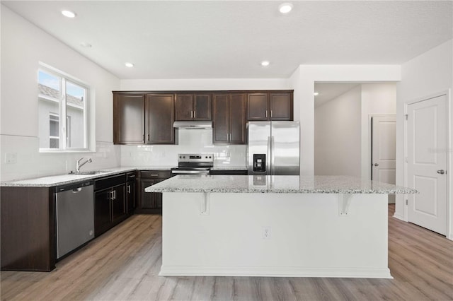 kitchen featuring appliances with stainless steel finishes, sink, a kitchen bar, a center island, and light hardwood / wood-style flooring