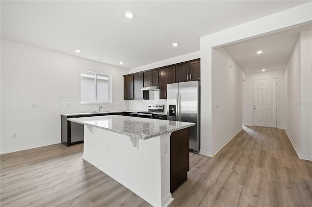 kitchen featuring stainless steel appliances, a center island, light stone counters, light hardwood / wood-style floors, and a kitchen bar