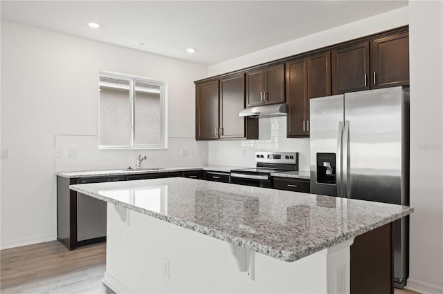 kitchen with sink, stainless steel appliances, a center island, tasteful backsplash, and light stone countertops