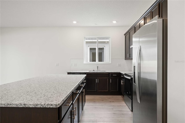 kitchen featuring appliances with stainless steel finishes, sink, a center island, light stone counters, and light hardwood / wood-style flooring