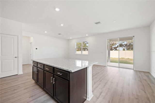 kitchen featuring dark brown cabinetry, light stone countertops, light hardwood / wood-style floors, and a kitchen island